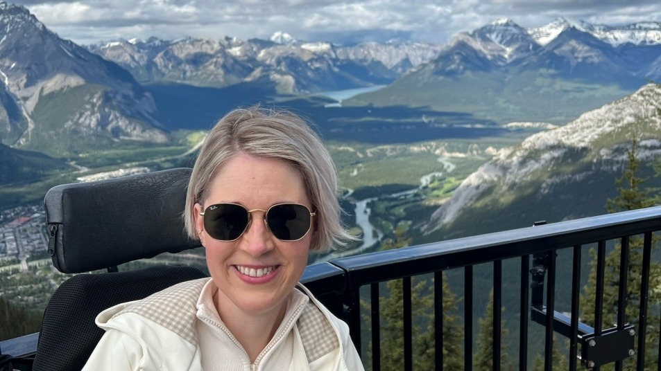 A woman sitting in a wheelchair overlooking the town of Banff, Alberta with the mountain ranges and rivers behind her.