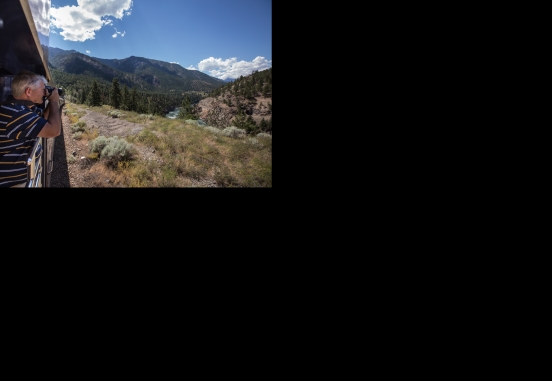 man takes a picture of the mountainous scenery while onboard rocky mountaineer train